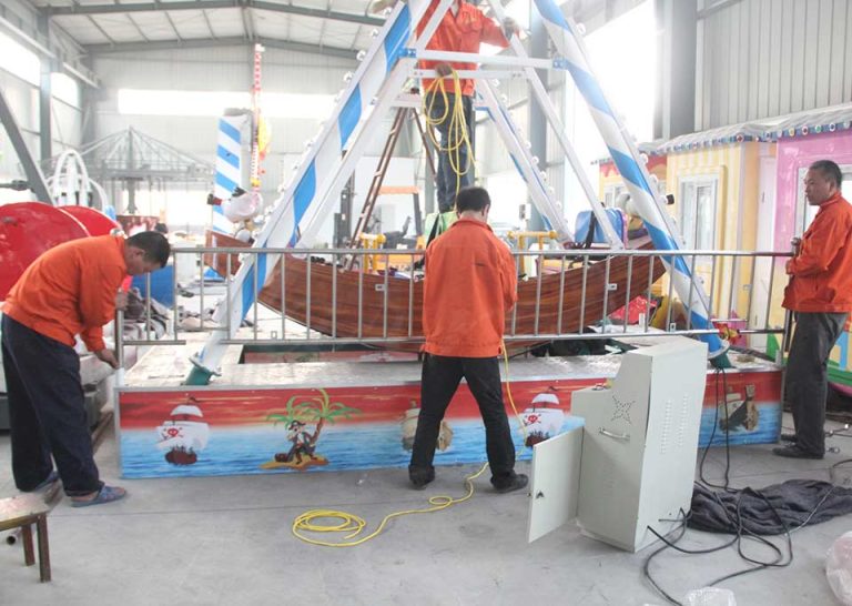 Workers installing a 10-seat mini pirate ship ride in a factory setting.