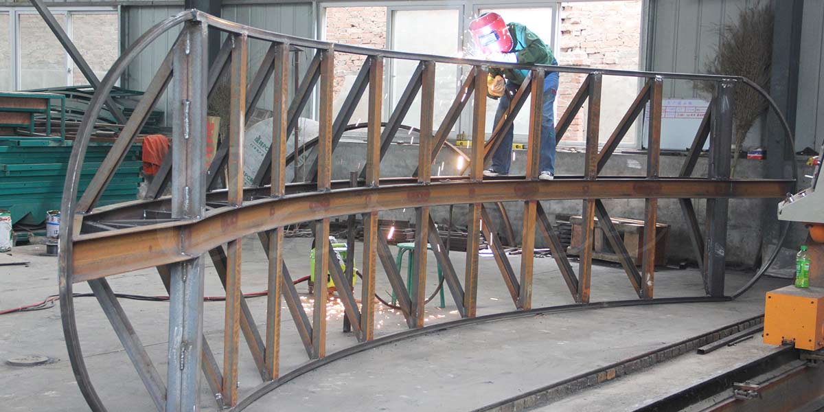 Worker welding steel frame structure of 16 seat pirate ship amusement ride in factory workshop
