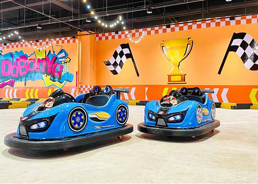 Two blue battery bumper cars with racing theme design at indoor amusement park.