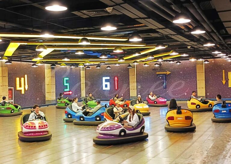 Crowd enjoying battery bumper cars ride on polished indoor track with colorful lighting.
