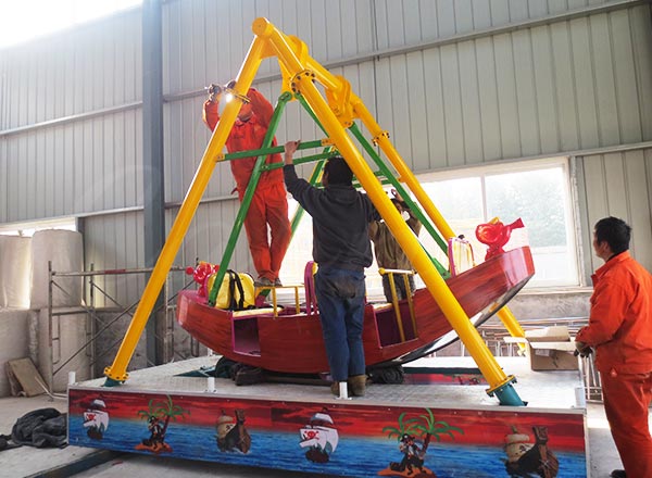 Technicians installing 12 seat mini kiddie pirate ship ride with colorful support structure