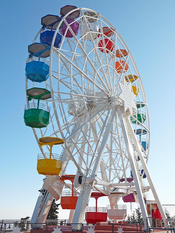 A colorful Ferris wheel with vibrant cabins in rainbow colors, set against a bright blue sky, at an amusement park.