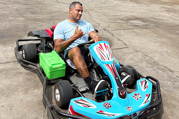 Brazilian client test-driving a green battery-powered go-kart at Carnee Rides outdoor test area.