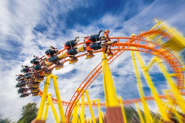 Inverted roller coaster with yellow tracks and orange supports, showing riders experiencing a thrilling upside-down turn under a blue sky.