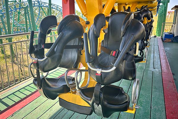 Close-up of ergonomic suspended roller coaster seats with advanced safety harness and restraint system.