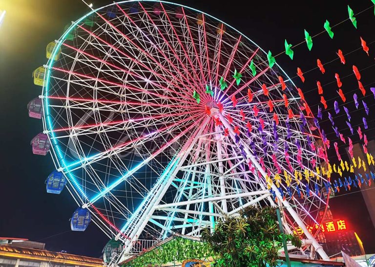Nighttime aerial view of a 49-meter Ferris wheel illuminated with colorful LED lights, showcasing its grandeur in an amusement park setting.