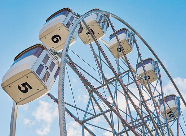 A close-up of Ferris wheel gondolas against the blue sky, showing several cabins in motion.