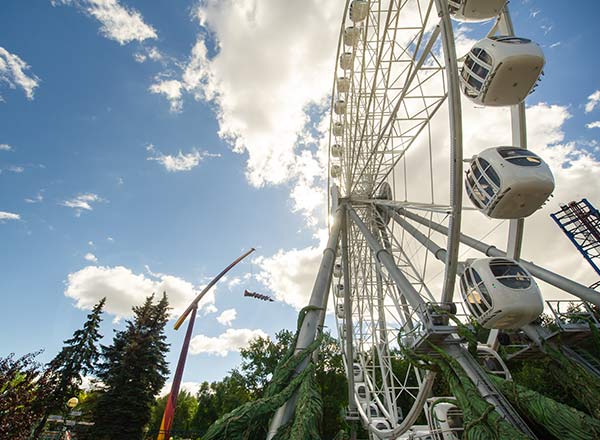 Ferris wheel at an amusement park with a scenic backdrop and cloudy sky, showcasing the spinning cabins.