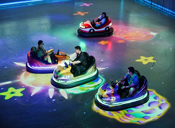 Visitors enjoying indoor bumper car rides with glowing LED floor projection in an amusement park.