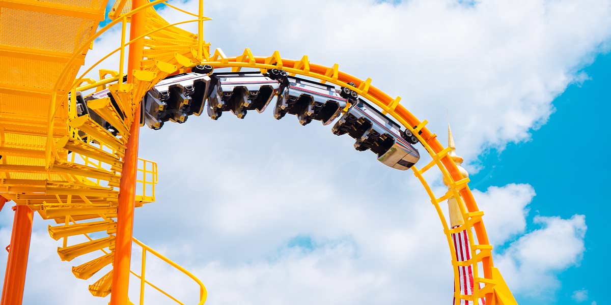 Yellow roller coaster inversion with riders upside down against blue sky