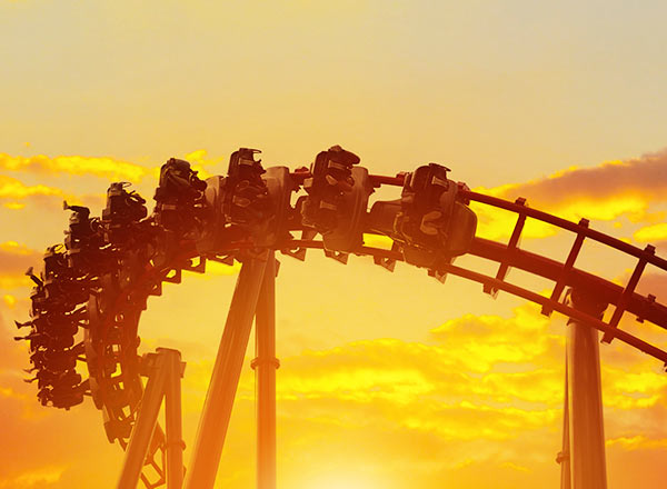 Roller coaster ride silhouette with riders during golden sunset