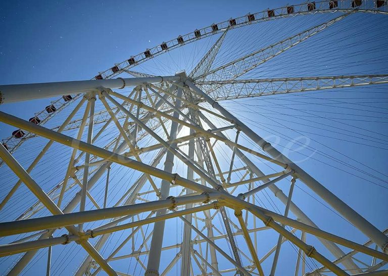 Vista hacia arriba de la estructura de acero de la noria de 120 m y las cabinas de pasajeros bajo la luz del sol
