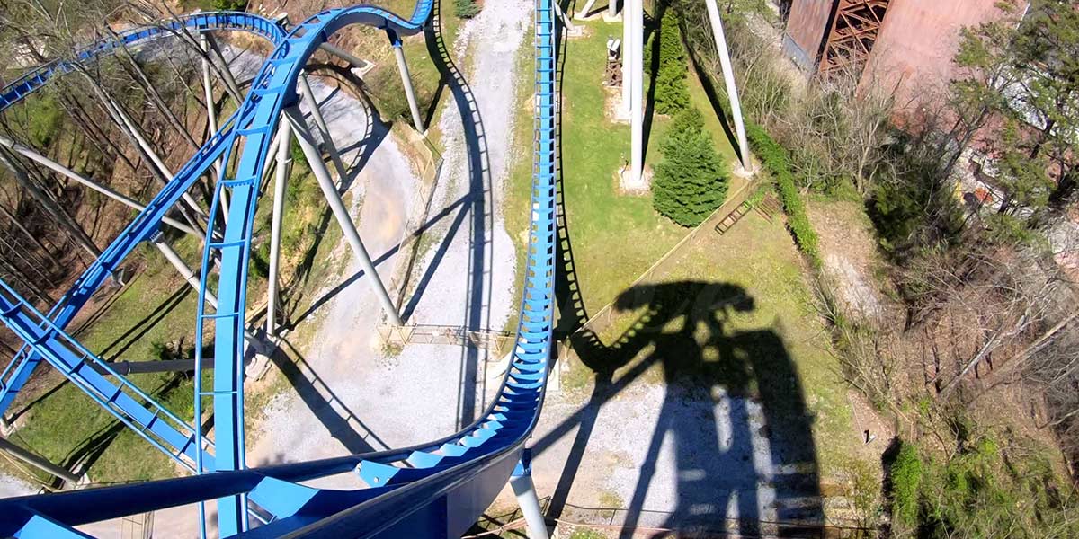 Blue steel backyard roller coaster track with steep drop and support columns casting shadow