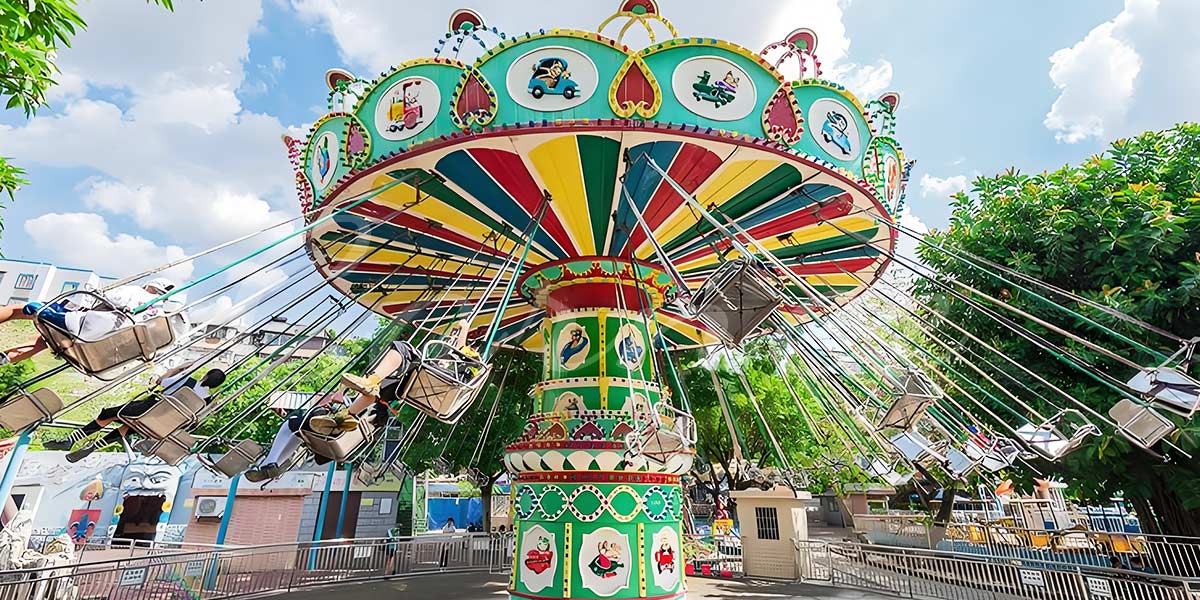 Colorful swing carnival ride operating in an amusement park during the day, with riders enjoying the rotation and outward swing motion.