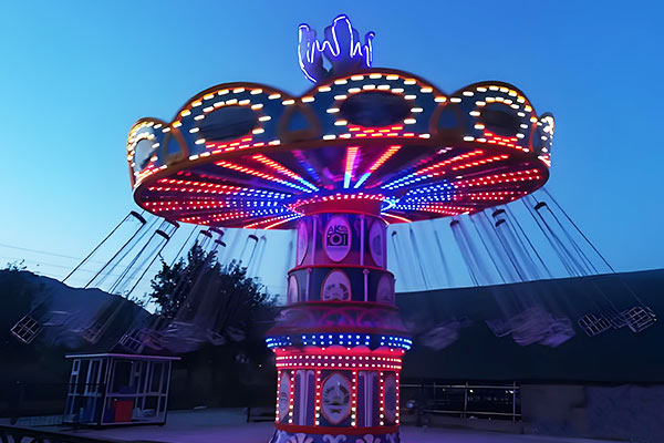 Balançoire de carnaval colorée avec lumières LED tournant la nuit dans un parc d'attractions