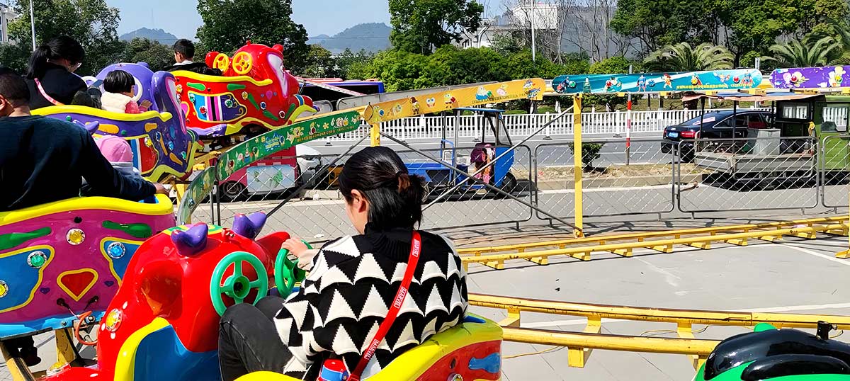Families and kids riding a small children’s roller coaster outdoors