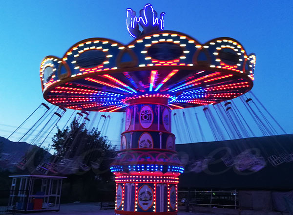 Classic illuminated wave swinger ride in amusement park at dusk, reflecting the nostalgic charm of traditional swing rides.
