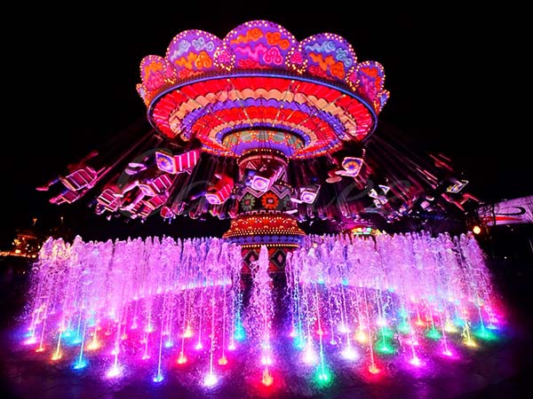 Customized swing carnival ride at a theme park, featuring decorative canopy and colorful chairs designed to match specific park themes.