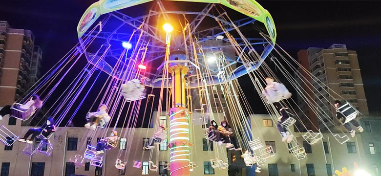 Different types of swing carnival rides on display in an amusement park, including rotating swings, tower swings, wave swingers, and deluxe models
