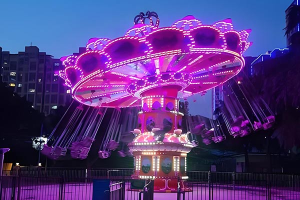 Chaise volante et balançoire avec des lumières violettes à la fête foraine de nuit