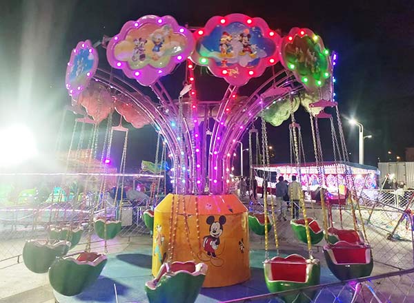 Colorful kiddie swing ride with cartoon decorations at night, showing how swing rides have evolved for children’s amusement.
