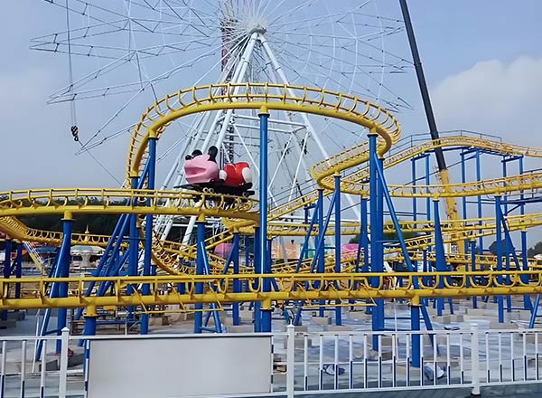 Mad Mouse roller coaster in amusement park with yellow track and ferris wheel background