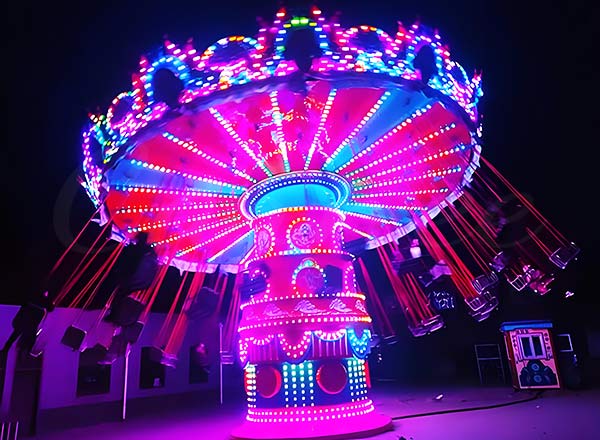 Neon-lit swing carousel ride at night, featuring dynamic and colorful lights, providing an exciting visual display and a fun ride experience at a carnival.