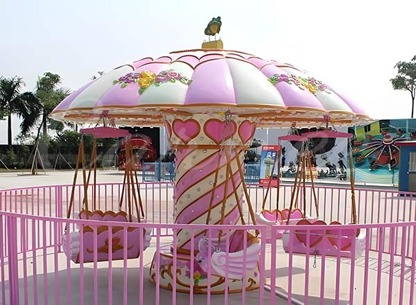Pink-themed carousel-style swing ride with heart decorations, designed for young children and families at amusement parks.