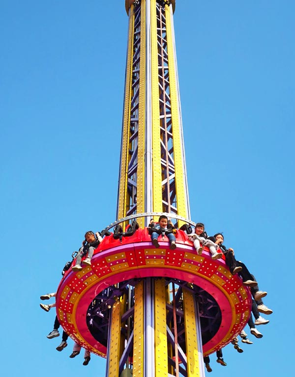 Drop tower ride at amusement park showing riders experiencing free fall from a tall tower under blue sky
