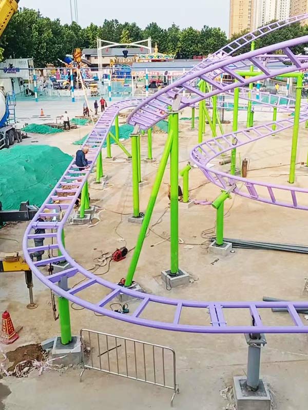 Family roller coaster track installation by Carnee Rides factory with purple and green supports at amusement park construction site.