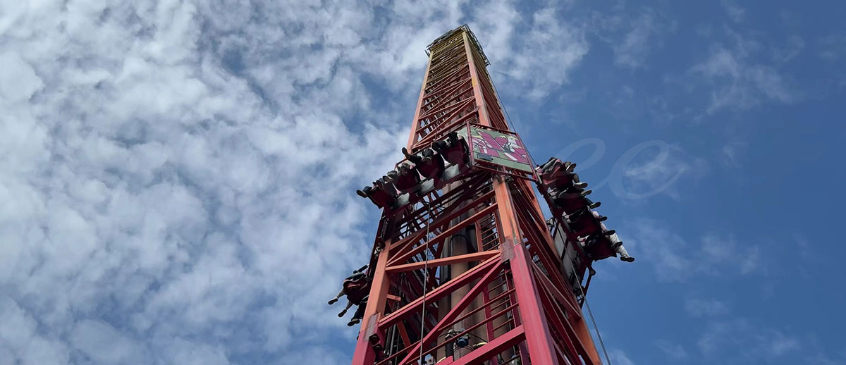 Giant red drop tower ride viewed from below showing riders at the top before the drop.