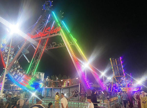 Colorful LED-lit pirate ship amusement ride operating at night, attracting crowds in a theme park