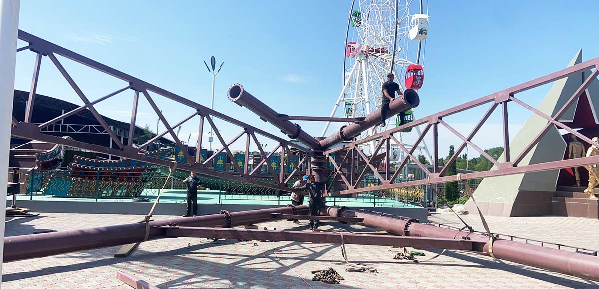 Workers assembling the steel structure of a large pirate ship ride during installation in an amusement park.