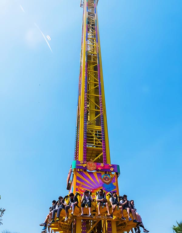 Close-up view of a colorful drop tower ride in a theme park with people ready to drop.