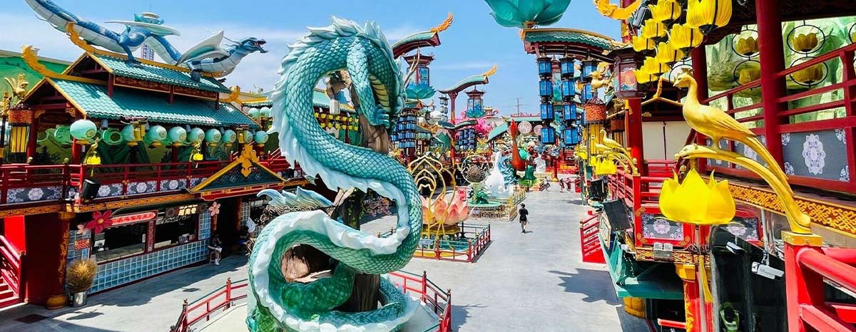 Decorações e esculturas com tema de dragão em um parque de diversões com visitantes explorando.