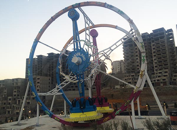 Vista exterior de una atracción de feria en forma de noria tras su instalación en Irak, mostrando la estructura de la atracción y el entorno del parque.