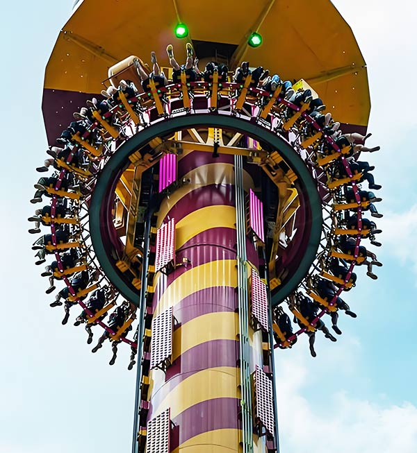 Крупный план полосатой башни Drop Tower, оснащенной вращающимся на 360 градусов кольцом для пассажиров. Эта дополнительная вращающаяся функция оправдывает более высокие цены на отдельные билеты и повышает общую рентабельность парка.
