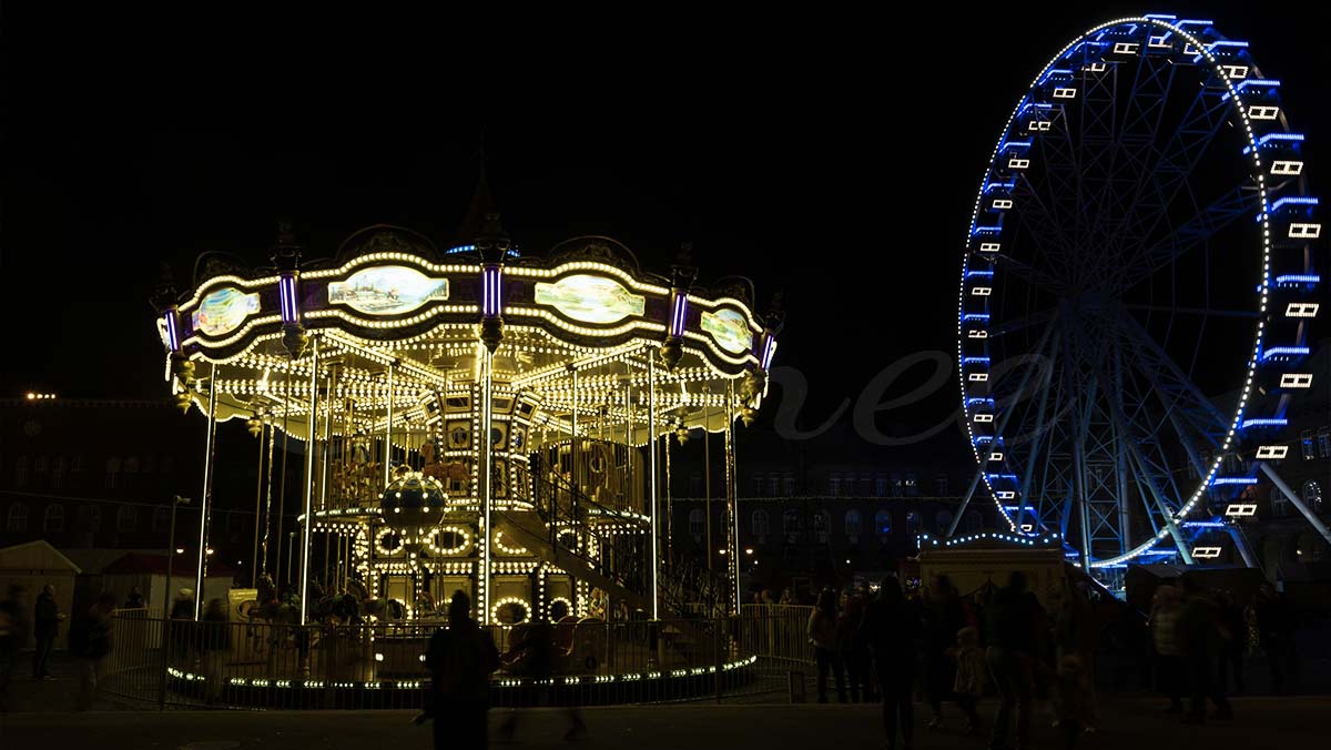 Un carrusel de lujo de dos pisos que funciona por la noche junto a una noria gigante, creando una atracción emblemática del parque de atracciones.