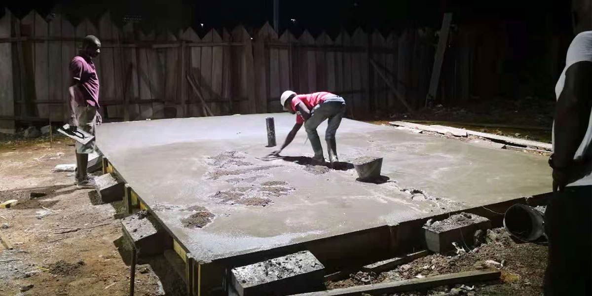 El hormigón fresco fluye desde la tubería tremie hasta el encofrado de los cimientos de la atracción durante la construcción en Camerún, donde un camión hormigonera estabiliza el suelo tropical para los cimientos de la torre de caída de Carnee Rides.