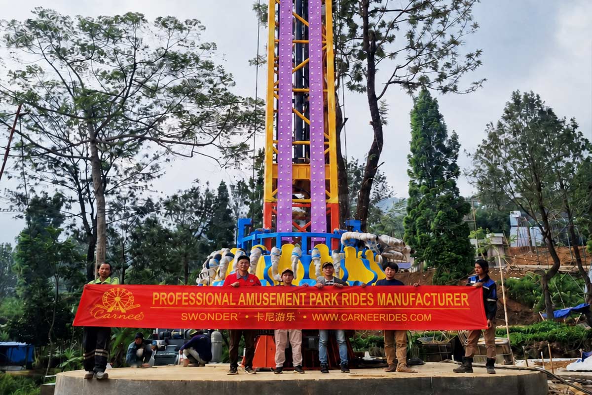 El equipo internacional de instalación de Carnee Rides y operadores de parques locales celebran la finalización con éxito de una atracción de torre de caída de 30 m, sosteniendo una pancarta en la que se lee Fabricante profesional de atracciones para parques de atracciones.