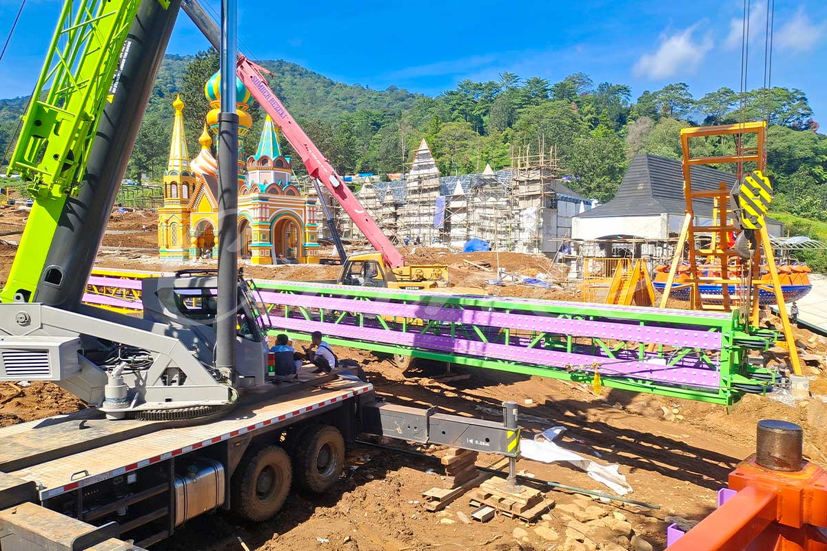 Grúa pesada que realiza el izado por secciones de una atracción de torre de caída libre de 30 m en un parque temático indonesio, demostrando una ingeniería de precisión milimétrica y una instalación profesional de atracciones de parque de atracciones.