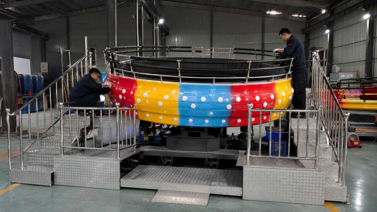 Inspección de mantenimiento en fábrica de la atracción Disco Tagada con técnicos que comprueban las barandillas, la plataforma, la estructura y las piezas mecánicas.