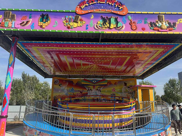 Manège disco Tagada fixe installé en extérieur avec auvent, barrière de sécurité, escaliers et décoration thématique colorée.
