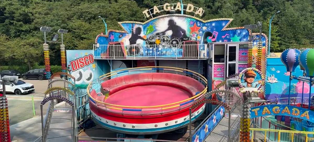 Manège extérieur Tagada installé dans un parc avec escaliers, plate-forme, barrière de sécurité et décor thématique