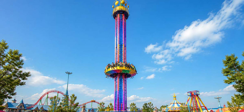 Guide d'achat d'une attraction commerciale de type « tour de chute libre » pour parc d'attractions, avec une tour haute, une nacelle circulaire, des lumières LED et un décor de parc à thème