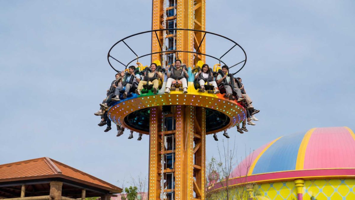 Gros plan sur la capacité d'accueil et les dispositifs de retenue d'une tour de chute libre, montrant les sièges circulaires, les harnais de sécurité, les passagers et la conception de la nacelle