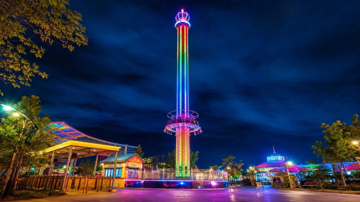 Manège de type « tour de chute » à LED pour une attraction nocturne de parc d'attractions, avec une tour illuminée, des lumières colorées, une nacelle circulaire et une ambiance de parc en soirée