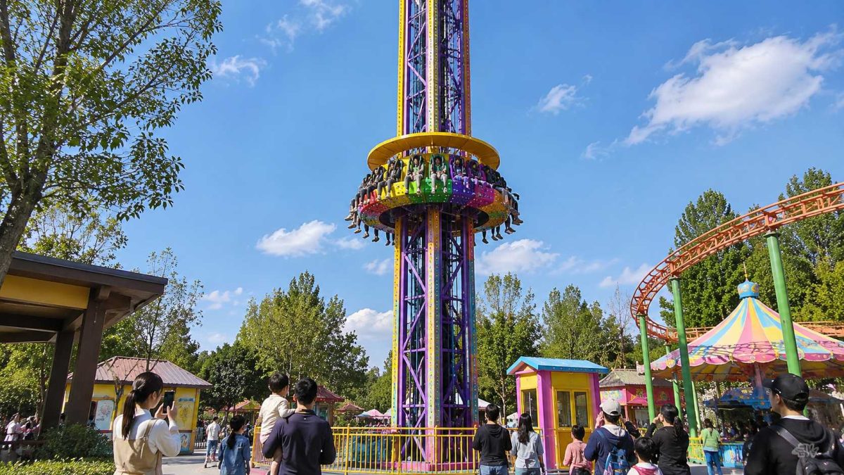 Manège de type « tour de chute rotative » dans un parc d'attractions, illustrant l'expérience des visiteurs, l'attrait pour les spectateurs et le design coloré de cette attraction en plein air