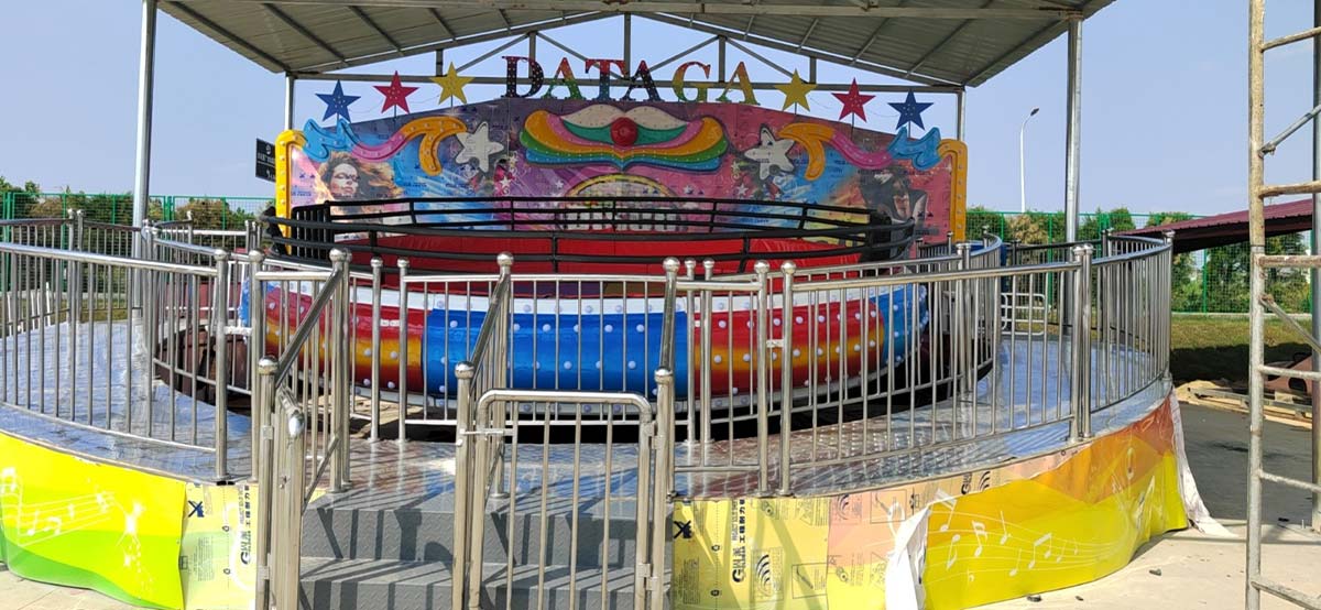 Manège « Commercial Disco Tagada » installé dans un parc d'attractions en plein air, équipé d'une plate-forme pour les passagers et d'un garde-corps de sécurité