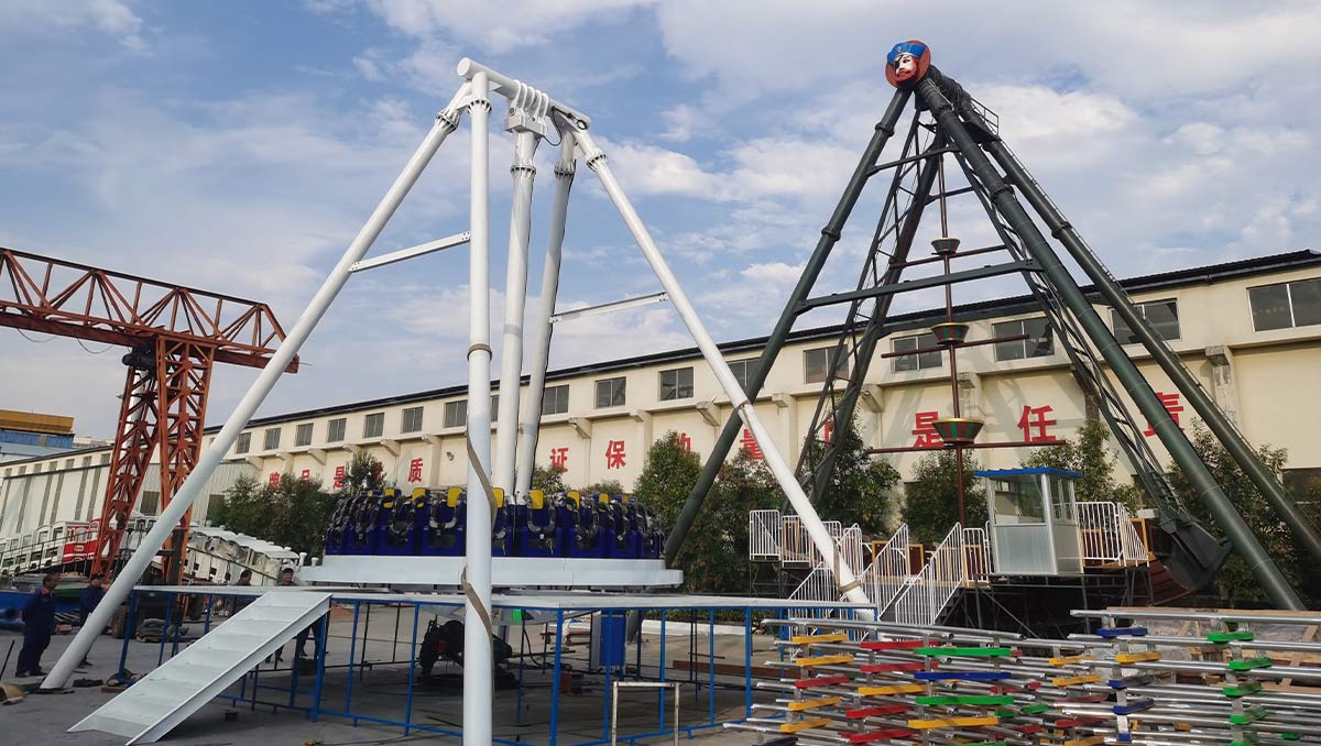 Montaje al aire libre en fábrica de una atracción tipo péndulo «Giant Frisbee» de alta resistencia, realizada por un fabricante certificado, en la que destacan el chasis de acero galvanizado y la estructura de cimentación fija.